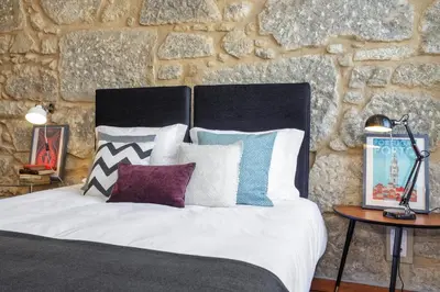 a bedroom with a bed with pillows and a stone wall at Oporto Chic & Cozy Studio Apartments in Porto