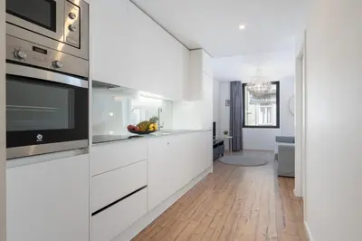 a kitchen with white cabinets and a wooden floor at Host Wise - Charming Welcoming Flat - Centrally Located in Porto