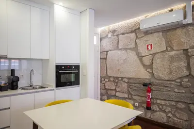 a kitchen with a white table and a stone wall at Mercadory Ribeira in Porto