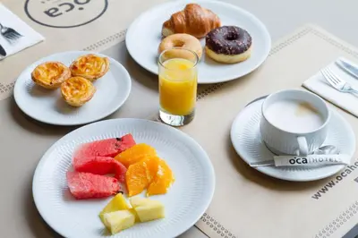 a table with plates of breakfast foods and a glass of orange juice at Bom Sucesso Hotel by gaiarooms in Porto