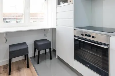 a kitchen with white cabinets and a stove and two stools at Cozy Studio-Fast Wi-Fi-Near Campanhã Station & River in Porto