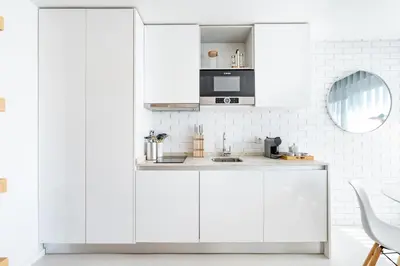 a white kitchen with white cabinets and a mirror at VIVA Marquês Studio in Porto