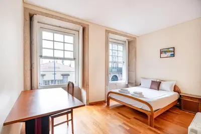 a bedroom with a bed and a table and two windows at VIVA Old Franciscan Studio in Porto
