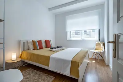 a white bedroom with a bed and a chair at Oliveira Monteiro Flat in Porto