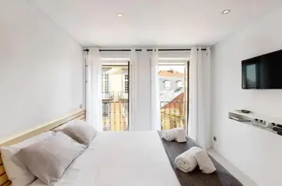 a white bedroom with a large bed and a flat screen tv at Cozy Studio city center in Porto
