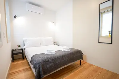 a bedroom with a bed with white sheets and a mirror at Mártires Sweet Apts by PortoCityHosts in Porto