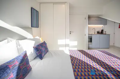 a bedroom with a white bed with pillows and a kitchen at Porto Formosa Central Lofts in Porto