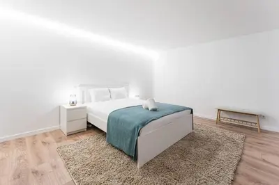 a white bedroom with a bed and a rug at Porto Paraíso Right by RDC in Porto