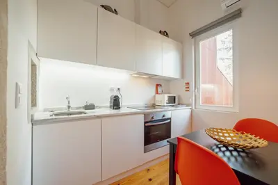 a kitchen with white cabinets and a table with red chairs at OPORTO GUEST Luxus Garden in Porto
