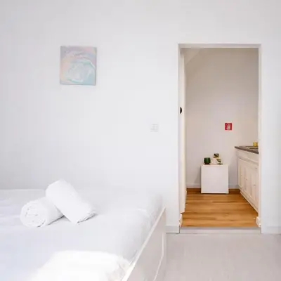 a white bedroom with a bed and a kitchen at PortoNest Downtown Suites in Porto
