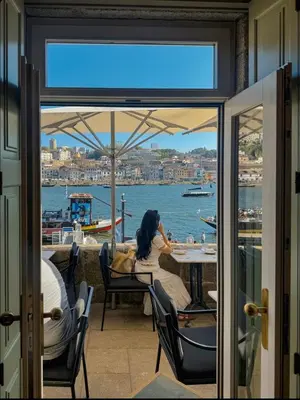 a woman sitting at a table with a view of the water at Porto Bello - Apartamento - 4 in Porto
