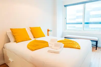 a white bed with yellow pillows and towels on it at Emotions Trindade Flat in Porto