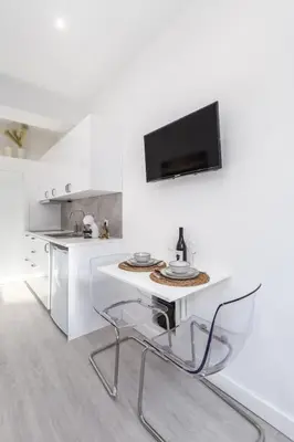 a white kitchen with a table and a tv on the wall at Studio de luxo no Porto - T0 in Porto