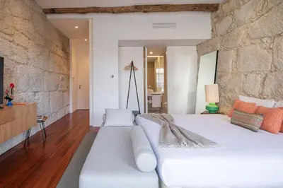 a bedroom with a white bed and a stone wall at Bandeiras in Porto