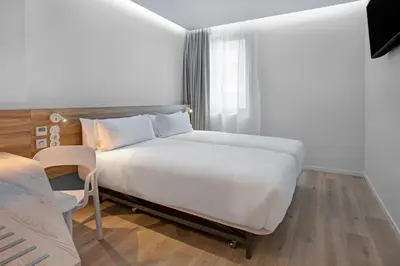 a bedroom with a large white bed and a chair at B&B HOTEL Porto Gaia in Vila Nova de Gaia