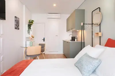 a bedroom with a white bed and a kitchen at C&P Bolhão Downtown Studio in Porto