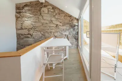 a room with a stone wall and a white table and chair at Alegria Duplex by Hosty in Porto