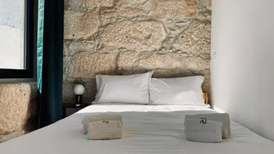 a bed with two pillows on it with a stone wall at Raul Dória - Guesthouse in Porto