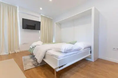 a white bedroom with a bed and a flat screen tv at Grandma aparts in Porto