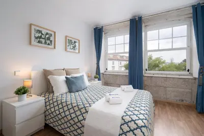 a bedroom with a bed with blue curtains and a window at Host Wise - Enchanting Unique Flat - Ace Location in Porto