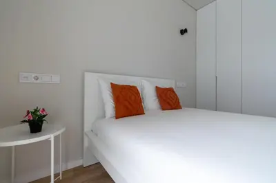 a white bedroom with a large bed with orange pillows at Bolhão Market Apartment in Porto