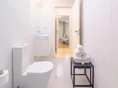 a white bathroom with a toilet and a table with towels at Charming 1-bedroom apartment in Porto in Porto