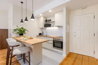 a kitchen with white cabinets and a wooden island with bar stools at Albertina Carlos Alberto by Aspasios in Porto