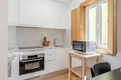 a kitchen with white cabinets and a microwave and a table at Host Wise Stylish Studio with Garage in Porto