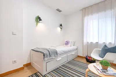 a white bedroom with a bed and a chair at Boavista Residence T3 in Porto