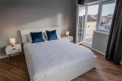 a white bed with blue pillows in a room with a window at 3BR Flat by Casa da Música, Central, Sleeps 6, 2D in Porto