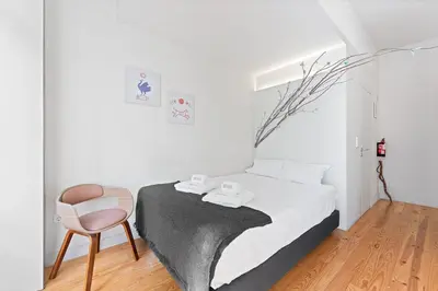 a white bedroom with a bed and a chair at GuestReady - Homely experience in Porto in Porto