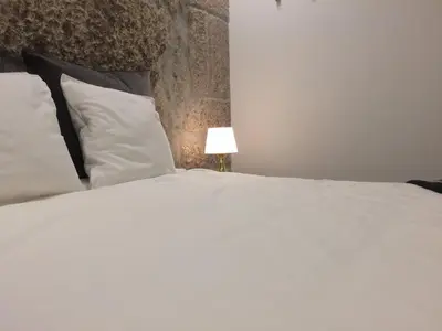 a bed with white sheets and pillows and a lamp at An apartment with a view - Nó's place in Vila Nova de Gaia