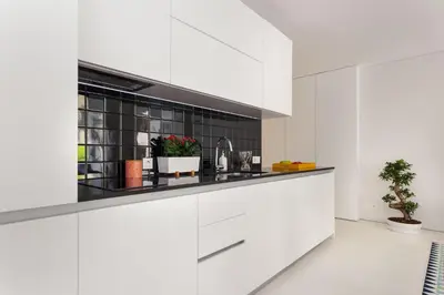 a kitchen with white cabinets and a black tile wall at PortoWhite city lofts in Porto