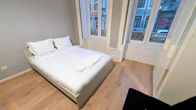 a small bed in a room with two windows at Riko Guest House 2 in Porto