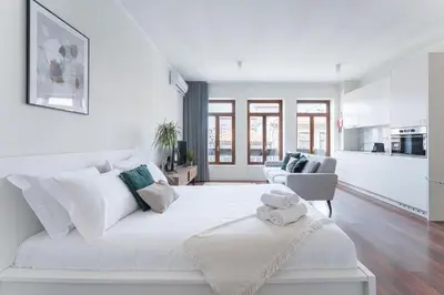 a white bedroom with a large white bed and a kitchen at Studio-Fast Wi-Fi- AC -5 min Trindade Metro&Clérigos in Porto