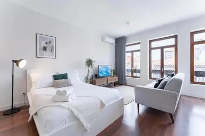 a white bedroom with a large bed and a chair at Studio-Fast Wi-Fi- AC -5 min Trindade Metro&Clérigos in Porto