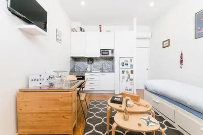 a small room with a bed and a table and a kitchen at Cantinho do Porto - Metro 1 Minute Away in Porto