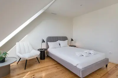 a white bedroom with a bed and a chair at GuestReady - Urban retreat in Boavista in Porto