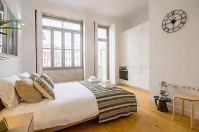a white bedroom with a large bed with a clock on the wall at Porto Pacific - Almeida Garrett - estúdio a 5 minutos da Ribeira in Porto