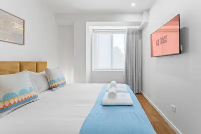 a bedroom with a large white bed with a blue blanket at GuestReady - Marble Root in Porto
