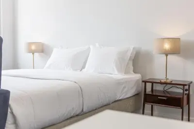 a white bed with white pillows and a table with two lamps at Porto República Suites in Porto