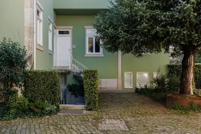a green house with a white door and a tree at Cozee Camões in Porto