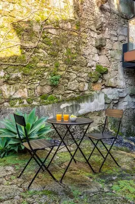 a table and two chairs in front of a stone wall at Modern & Cozy Flats with Terrace by HostWise in Porto
