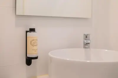 a white bathroom with a bottle of soap next to a sink at Uma Poveiros in Porto