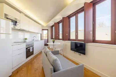 a kitchen with white cabinets and a couch and a tv at Try Oporto - São Lázaro in Porto