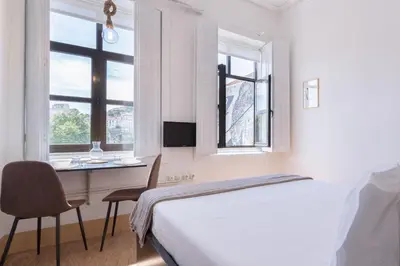 a bedroom with a bed and a desk and windows at Goabio Studio River View in Porto