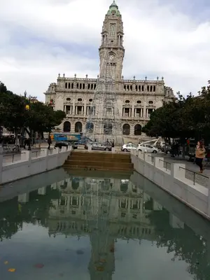 a clock tower in front of a building with a reflection in the water at daPraça Apartments in Porto