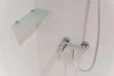 a shower with a hose in a white tiled bathroom at GuestReady - Mezzanine at the Bridge in Porto