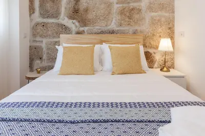 a bedroom with a white bed with a stone wall at Sendme2Portugal: Loureiro in Porto