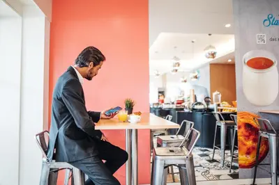 a man sitting at a table in a restaurant looking at his cell phone at Stay Hotel Porto Centro Trindade in Porto